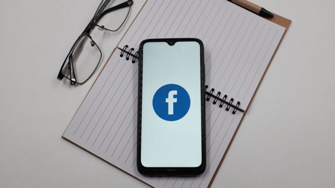 In this photo illustration a Facebook logo is displayed on a smartphone screen above a notebook next to glasses in Athens, Greece on April 4, 2023. Meta Platforms has canceled Jada Pinkett-Smith's show ‘Red Table Talk' due to Meta getting rid of its original programing. NIKOLAS KOKOVLIS/BENZINGA