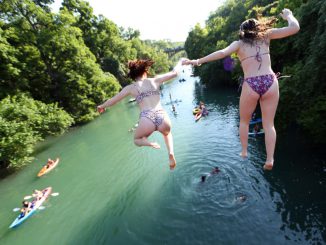 Residents jump off a bridge while swimming, paddle boarding and kayaking in Barton Creek on May 20, 2020 in Austin, Texas. (Photo by Tom Pennington/Getty Images)