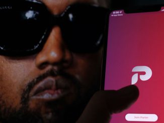 This illustration photo shows the Parler social network app logo on a cell phone screen with a picture of US rapper Kanye West in the background in Los Angeles, October 17, 2022. Parlement Technologies, owner of the self-described free speech social network, started the spate of layoffs in late November, according to The Verge's sources. CHRIS DELMAS/METANEWS