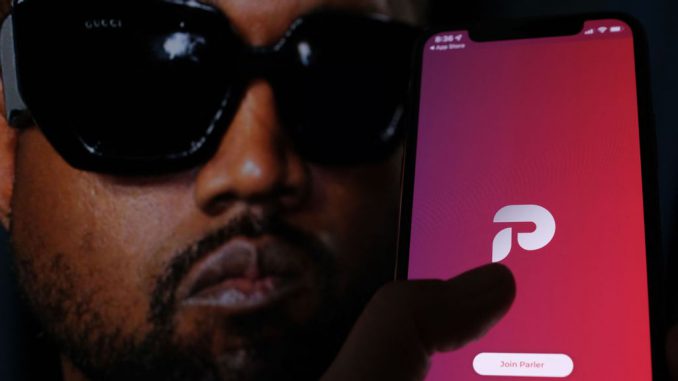 This illustration photo shows the Parler social network app logo on a cell phone screen with a picture of US rapper Kanye West in the background in Los Angeles, October 17, 2022. Parlement Technologies, owner of the self-described free speech social network, started the spate of layoffs in late November, according to The Verge's sources. CHRIS DELMAS/METANEWS