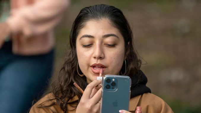 strongIN FILE -A woman uses her phone as a mirror while applying lipstick amid the coronavirus pandemic in Washington Square Park on April 09, 2021, in New York City. Regardless of age or gender, the research suggests that people spend a sixth of their lives enhancing their beauty.  ALEXI ROSENFELD/GETTY IMAGES/strong