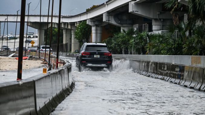 A car drives through the flooded street during heavy rain in Miami, Florida, on April 12, 2023. CHANDAN KHANNA/BENZINGA