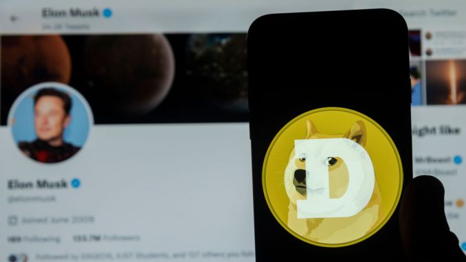 In this photo illustration, Dogecoin logo seen displayed on a mobile phone screen with Elon Musk's Twitter account in the background. Musk has been known to have price flucuations in markets through his tweets. IDREES ABBAS/BENZINGA