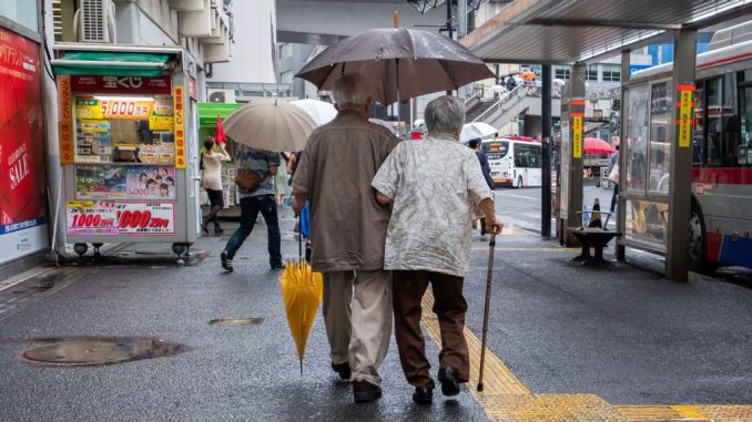 Old Japanese couple walking at a bus stop with umbrella during a rainy day, Shibuya, Tokyo on July 4th, 2018. SHUTTERSTOCK