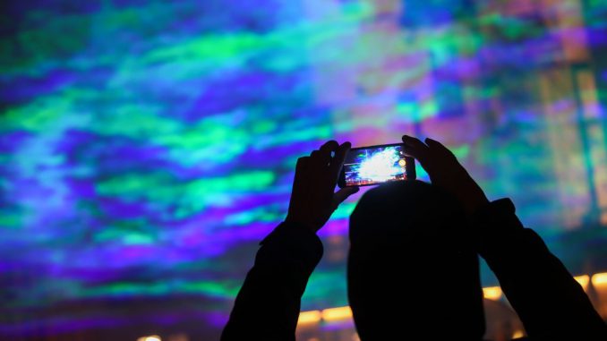 A passer-by takes pictures of artificially generated auroras on the Hallmarkt using laser beams and fog. The light installation entitled Borealis by Swiss artist Dan Archer is part of this year's Silver Salt Science and Media Festival. Under the motto Home Earth it will take place from October 14 to 18 in Halle (Saale). (Jan Woitas/picture alliance via Getty Images)
