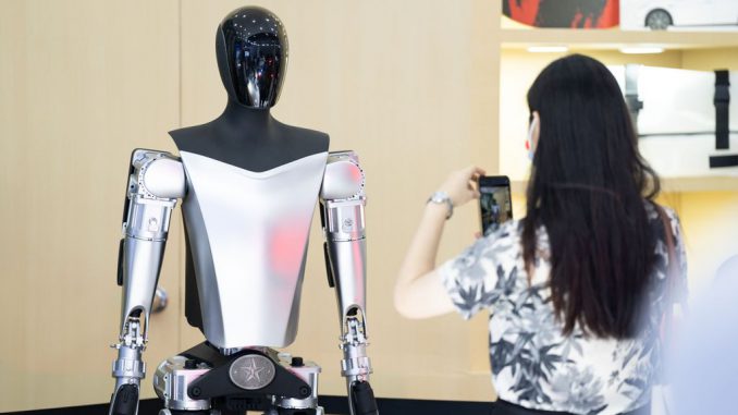 A visitor takes photos of Tesla's Optimus humanoid robot during the 2023 China International Fair for Trade Services (CIFTIS) at China National Convention Center on September 2, 2023 in Beijing, China. The bots employ additional sensing such as audio, proprioception, and temperature. VCG/VCG VIA GETTY IMAGES.